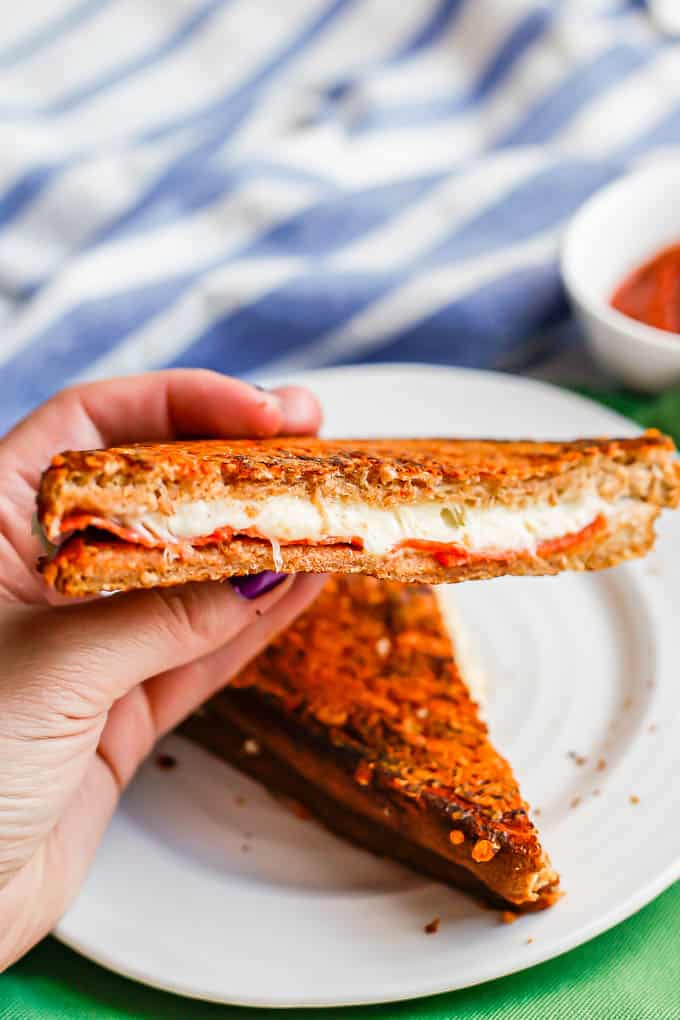 A hand holding up the cut side of a pizza grilled cheese sandwich from a white plate