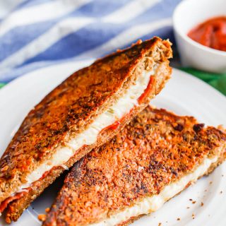 A crusted pizza grilled cheese sandwich with mozzarella and pepperoni cut in half and served on a white plate