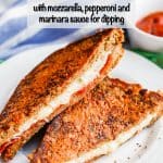 A crusted pizza grilled cheese sandwich with mozzarella and pepperoni cut in half and served on a white plate with a text overlay on the photo