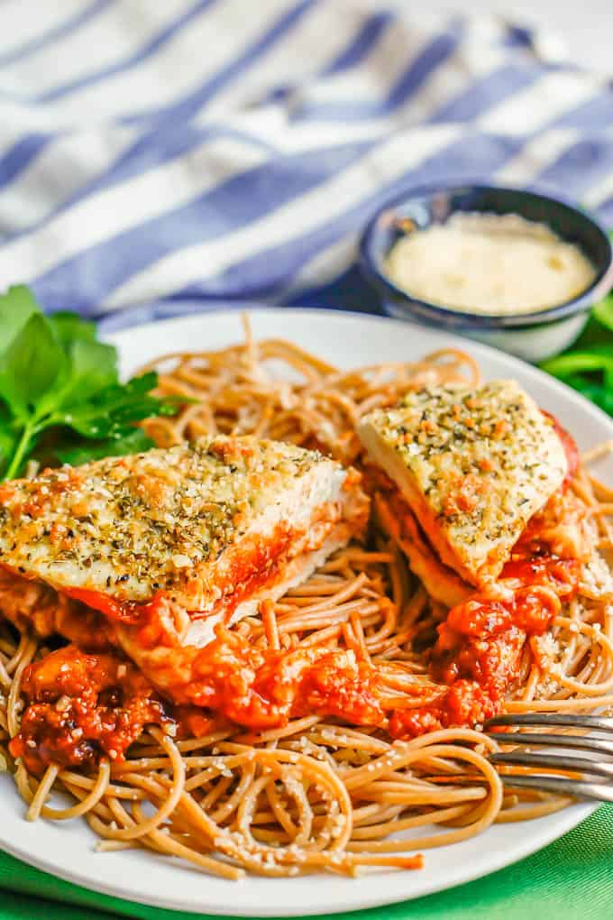 A pizza stuffed chicken breast cut in half and served over spaghetti with a fork resting on the plate