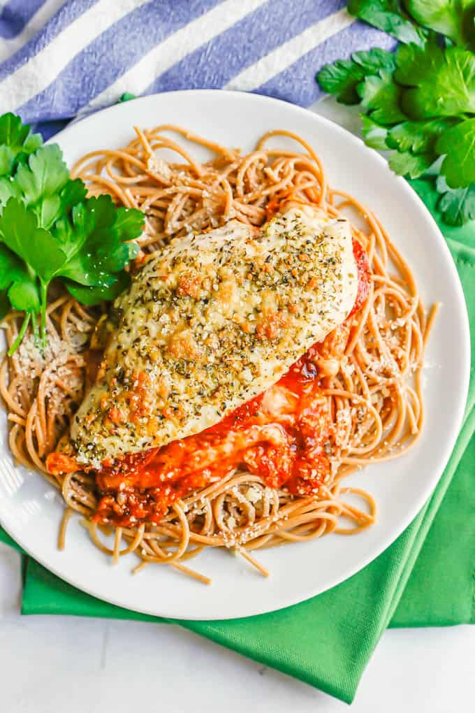 A white dinner plate with pizza stuffed chicken served over spaghetti