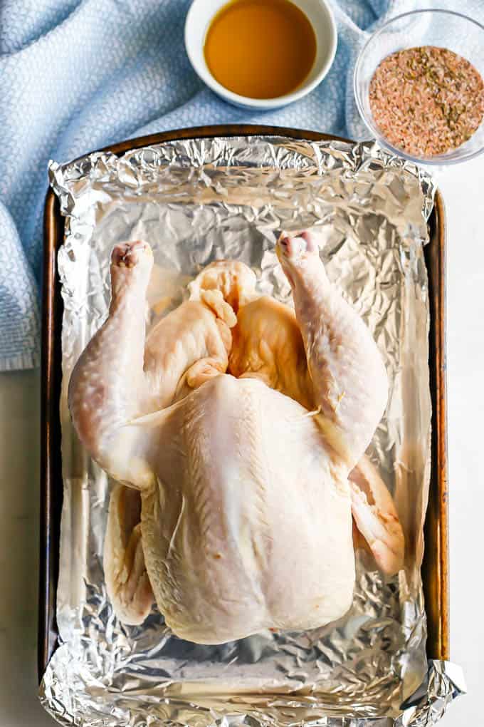 A whole chicken set in an aluminum foil baking pan before being seasoned and cooked