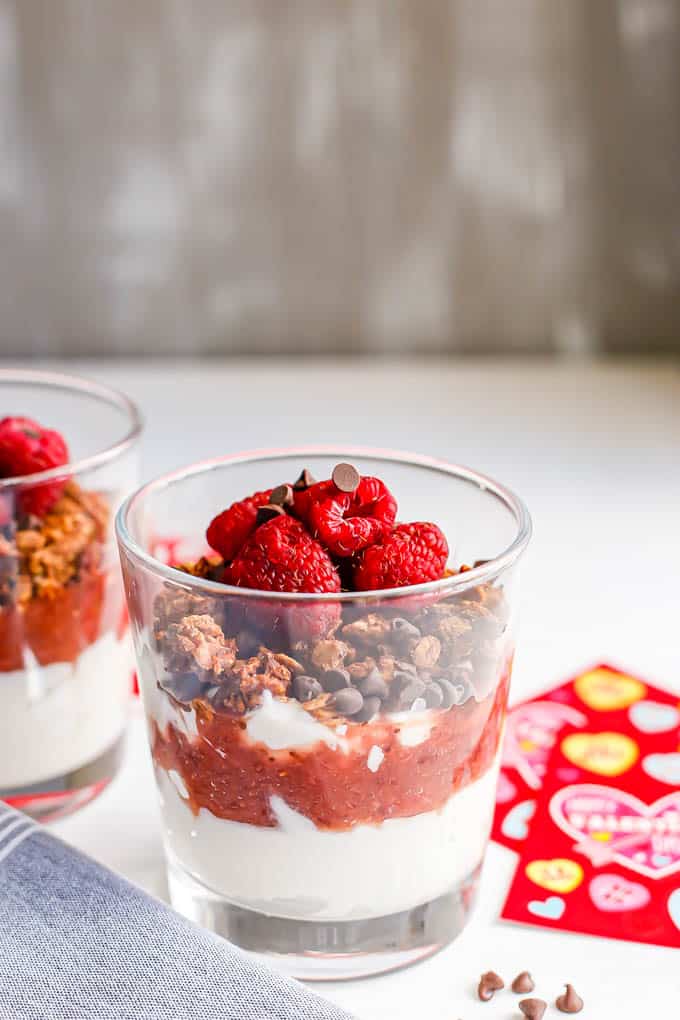 A red and white layered yogurt parfait with chocolate granola and chocolate chips