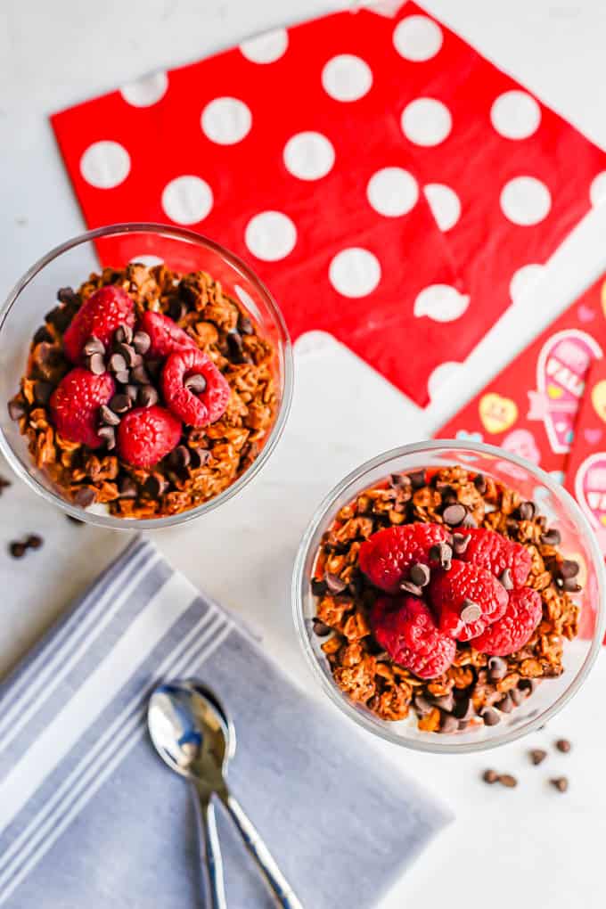 Overhead shot of yogurt breakfast parfaits with granola and berries and Valentine's Day napkins and cards nearby