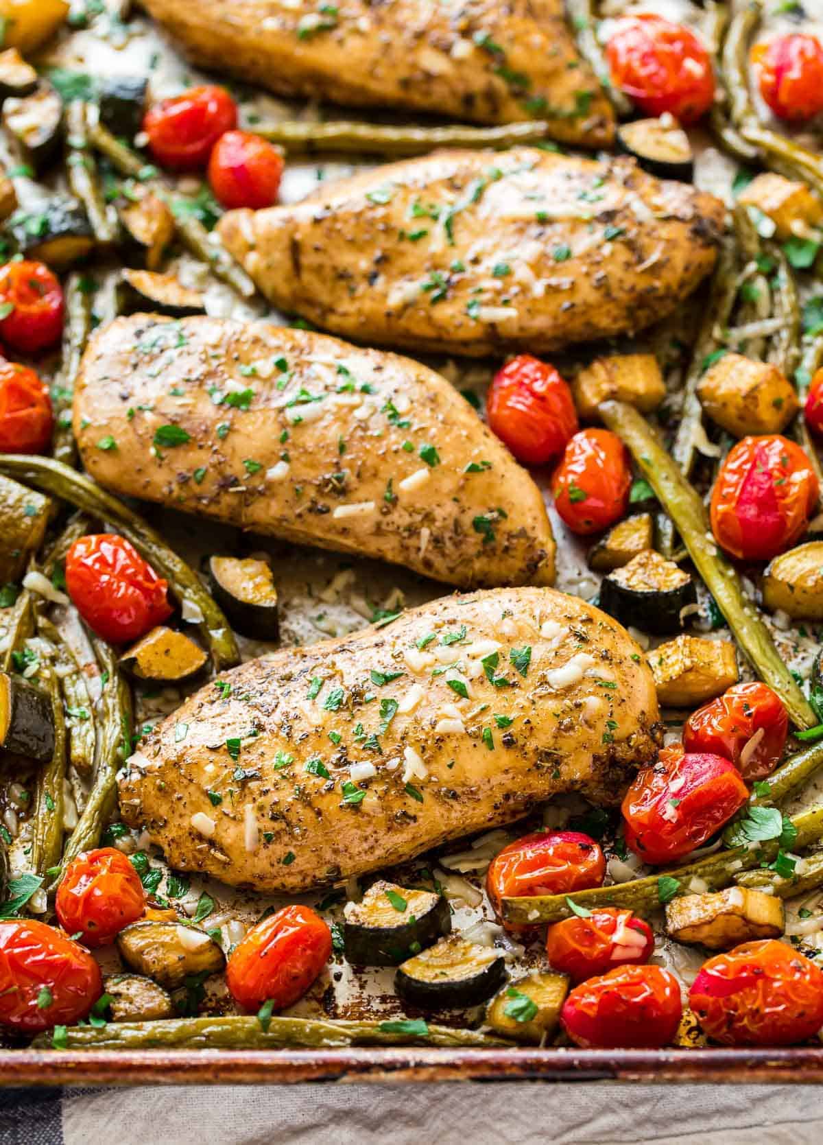 A sheet pan with baked chicken breasts and mixed vegetables seasoned with Italian seasonings