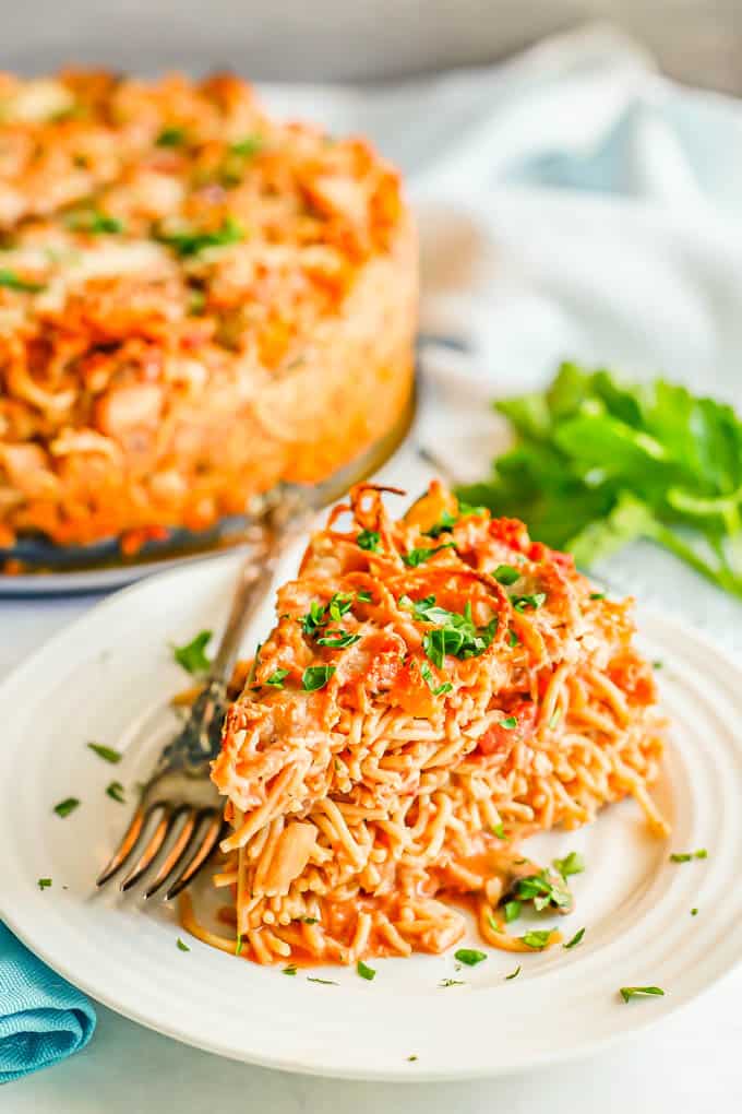 A slice of spaghetti pie served on a small white plate and topped with chopped parsley