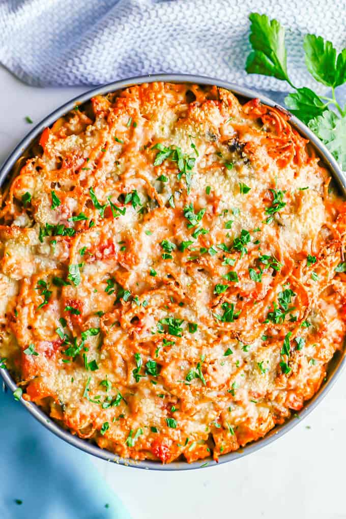 Baked chicken and veggie spaghetti pie in a springform pan with parsley sprinkled on top