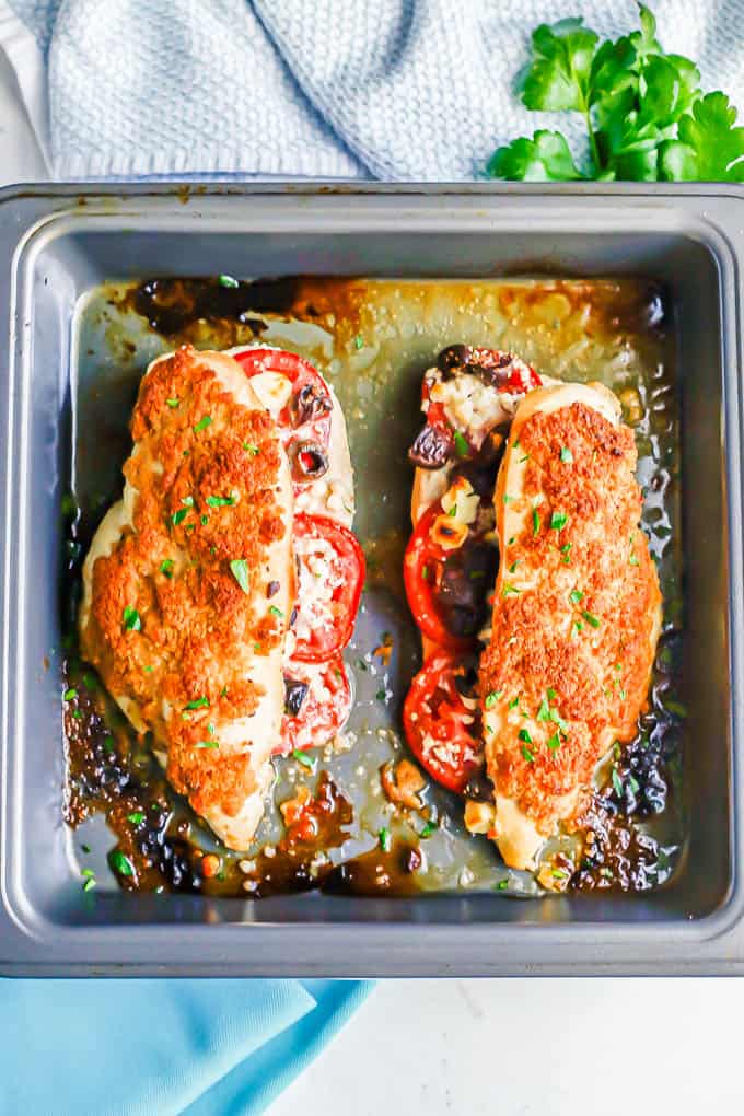 Two Greek stuffed chicken breasts with tomatoes, olives and feta cheese in a baking dish after roasting