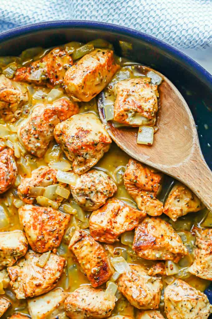 A skillet with saucy honey mustard chicken with onions and a wooden spoon scooping some up