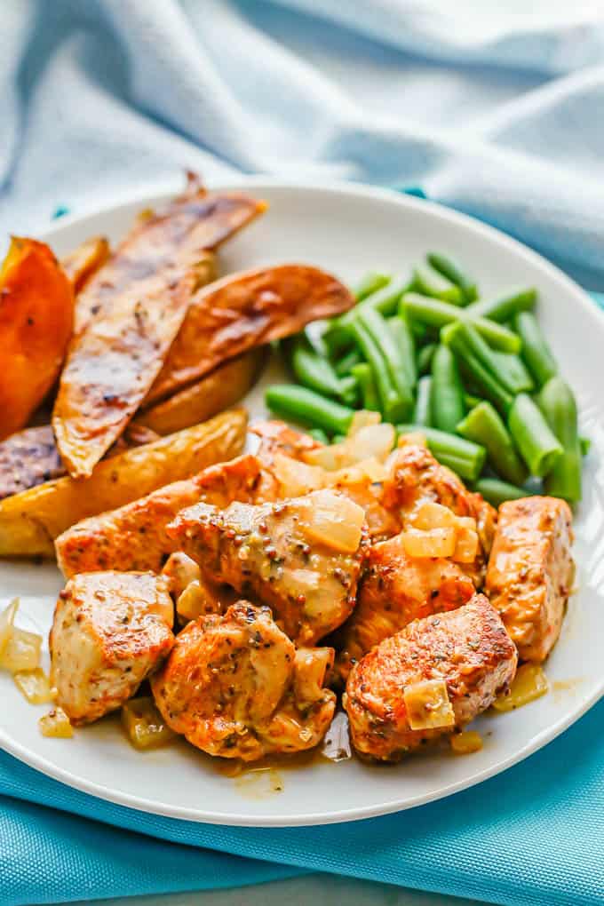 Close up of cubes of chicken with a honey mustard sauce on a white dinner plate