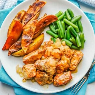 A white dinner plate with honey mustard chicken, roasted potato wedges and green beans with a fork alongside the plate