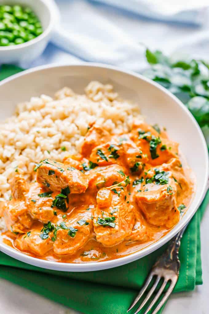 A low white bowl with steamed brown rice and Indian butter chicken with parsley sprinkled on top