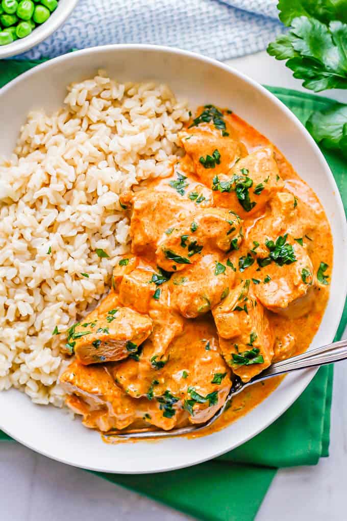 Instant Pot butter chicken served with rice in a low white bowl with a fork to the side and parsley sprinkled on top