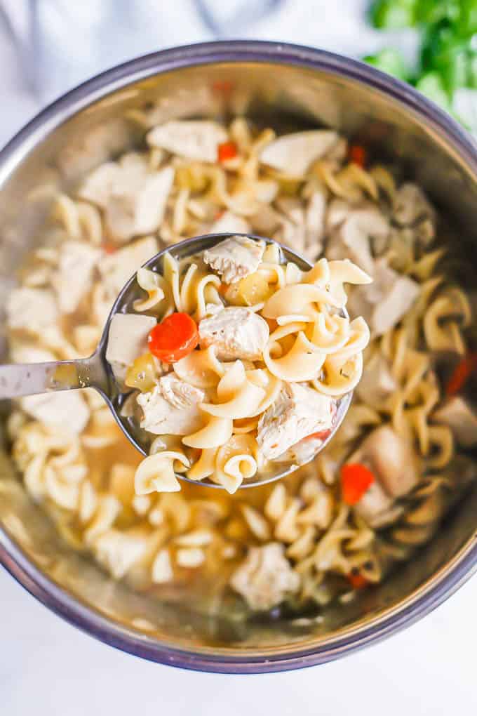 A ladle full of chicken noodle soup being lifted from an Instant Pot insert