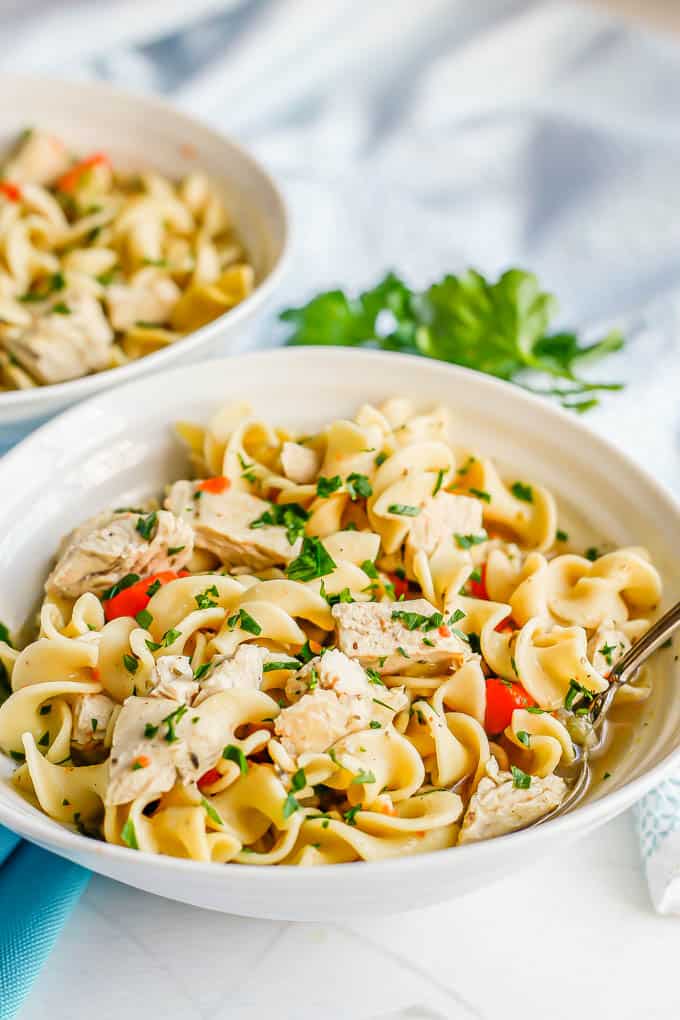 Two bowls of chicken noodle soup served with parsley sprinkled on top and a spoon resting in one of the bowls