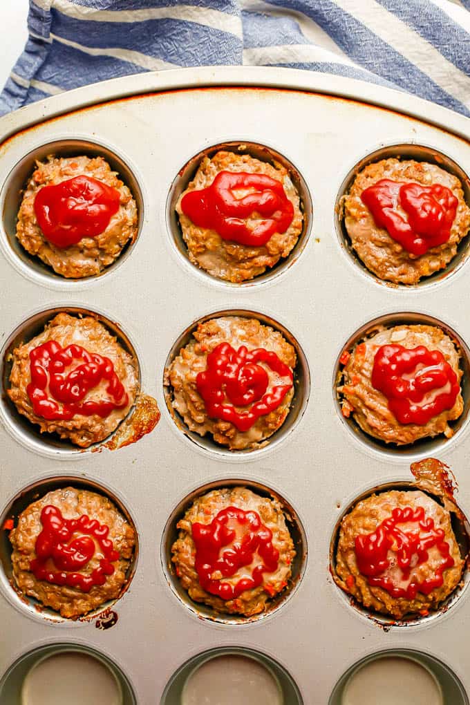 A muffin tin with 9 mini meatloaf muffins topped with ketchup after being baked