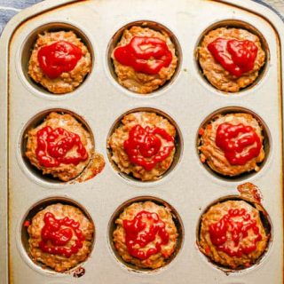 A muffin tin with mini meatloaves topped with ketchup after being baked