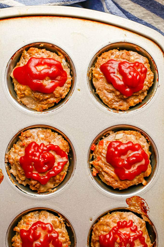 Mini meatloaf muffins in a muffin tin topped with ketchup