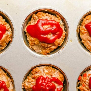 Close up of mini meatloaf muffins in a muffin tin topped with ketchup