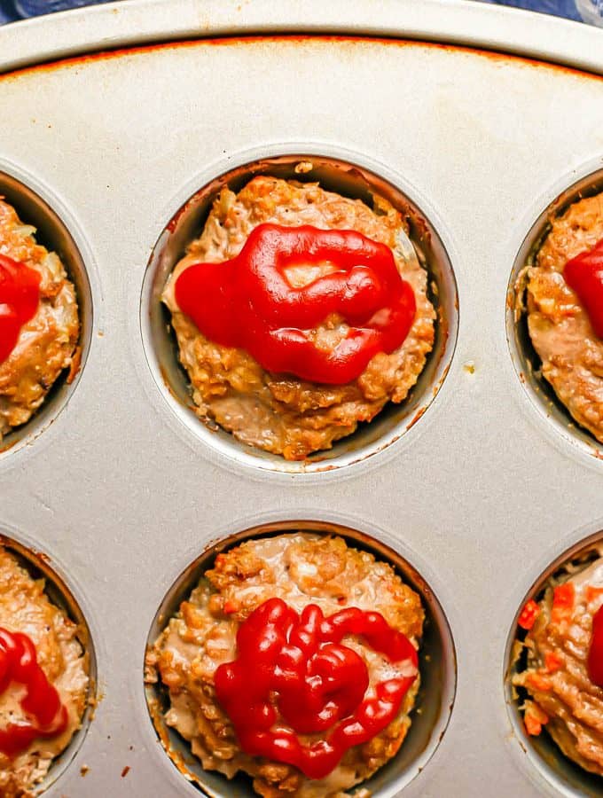 Close up of mini meatloaf muffins in a muffin tin topped with ketchup