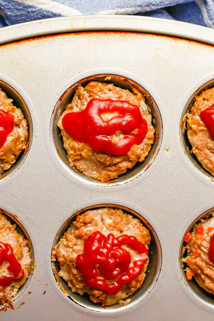 Close up of mini meatloaf muffins in a muffin tin topped with ketchup