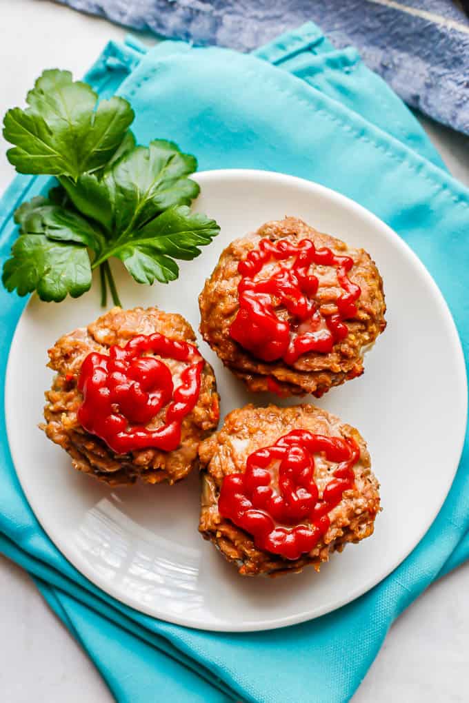 Ground turkey meatloaf muffins topped with ketchup and served on a white plate with a garnish of parsley