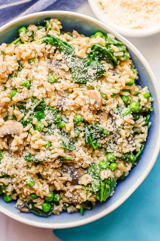 Close up of brown rice and veggies mixed together and served with Parmesan cheese in a blue and white bowl