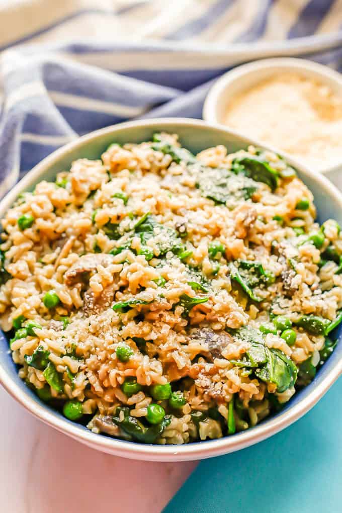 A large blue and white serving bowl of brown rice with vegetables topped with Parmesan cheese