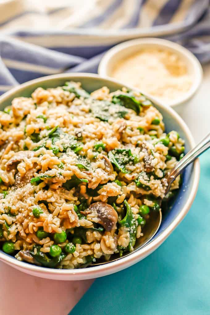 A serving spoon resting in a blue and white bowl of a brown rice and veggie mix