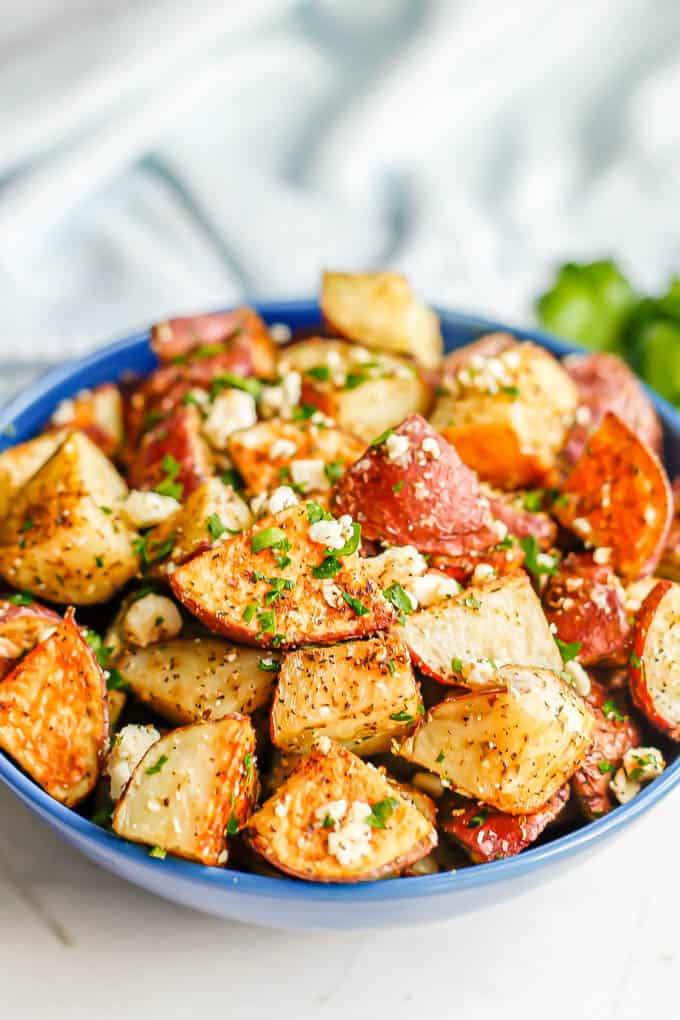 Greek roasted potatoes with feta and parsley served in a blue bowl