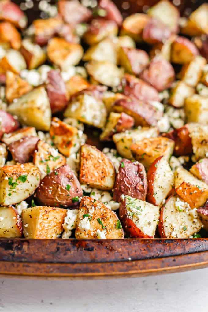 Close up of roasted red potatoes on a baking sheet with parsley and feta cheese