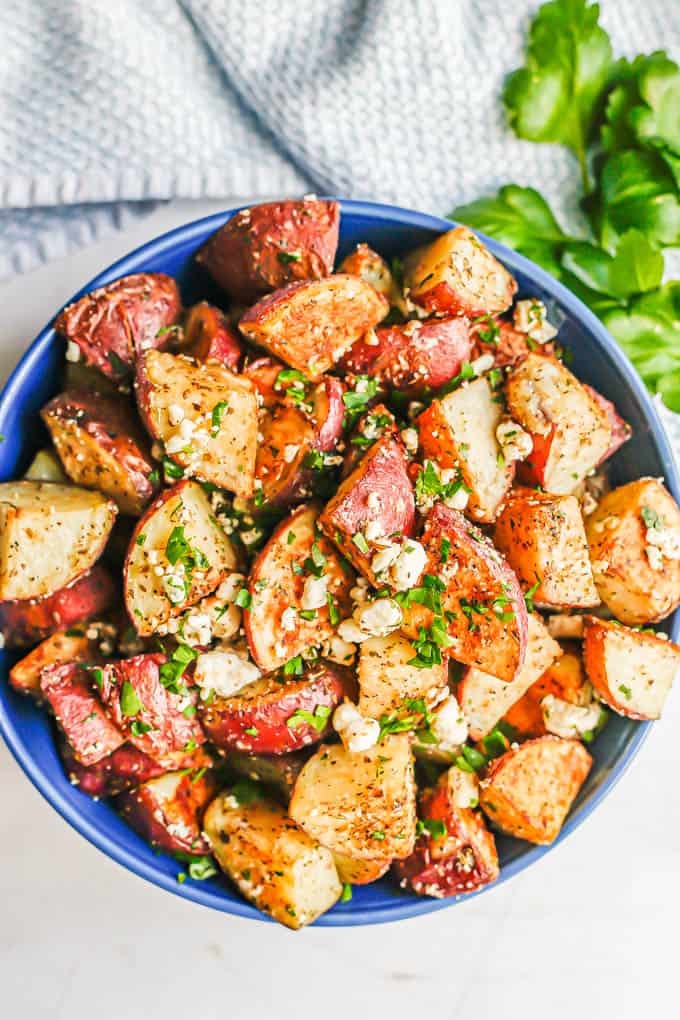 A blue bowl with roasted Greek potatoes mixed with feta cheese and fresh parsley