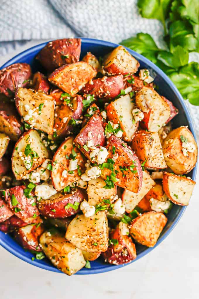 Overhead shot of Greek roasted potatoes with feta cheese and parsley served in a blue bowl with sprigs of parsley to the side