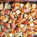 A sheet pan with roasted red potatoes mixed with feta cheese and fresh herbs and a text overlay on the photo