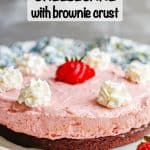 A dessert of strawberry cheesecake on a brownie crust plated on a white plate and topped with whipped cream with a text overlay on the photo