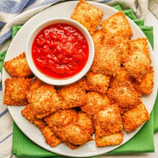 Overhead of a white plate with fried ravioli and a small white bowl of marinara sauce