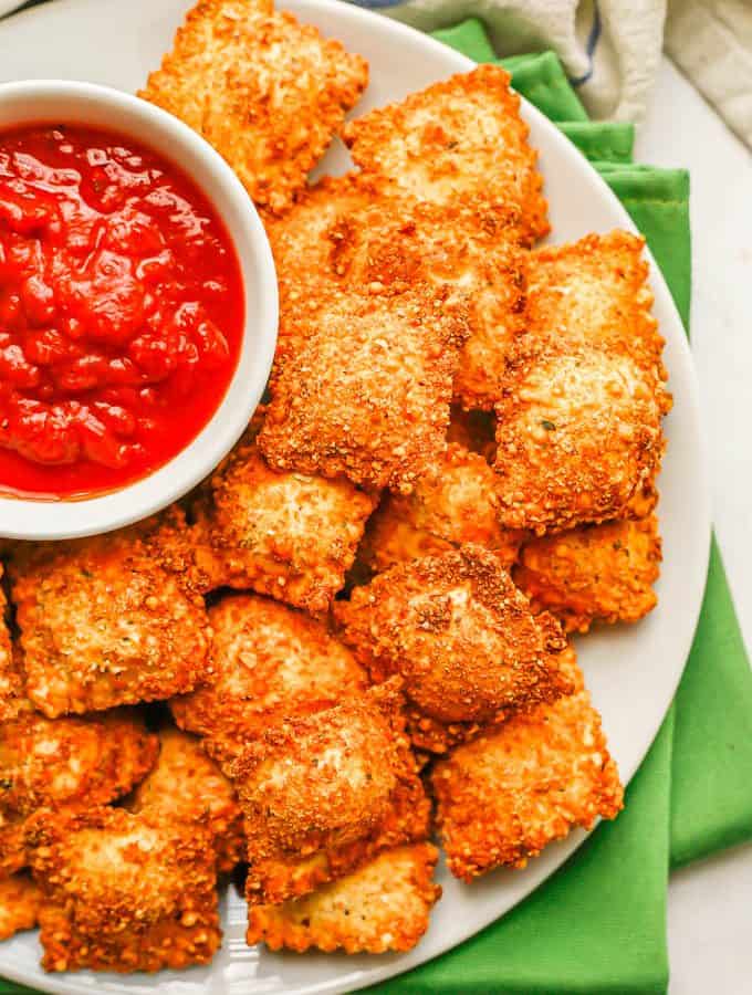 Close up of fried ravioli on a plate with a bowl of marinara