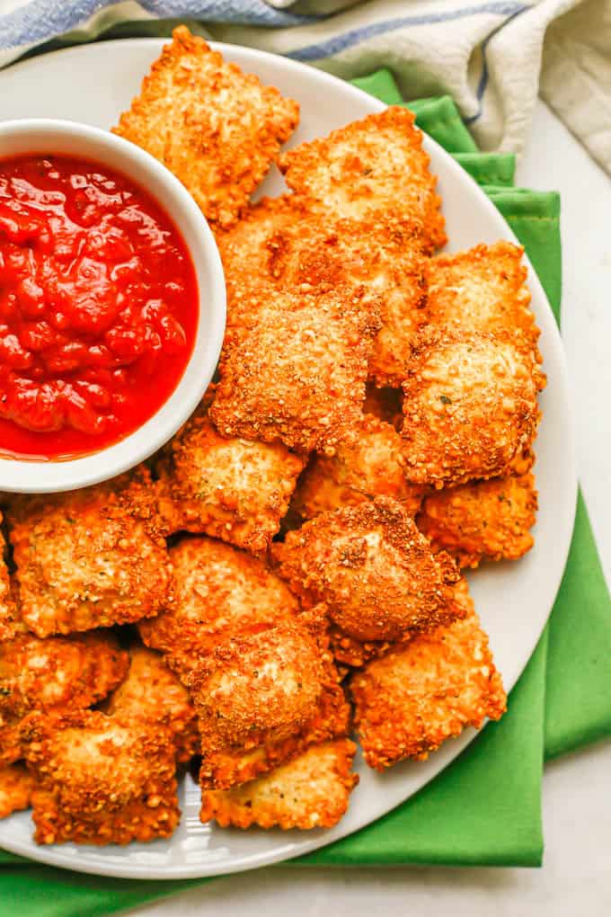 Close up of fried ravioli on a plate with a bowl of marinara