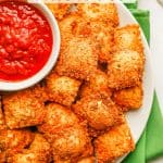 Close up of fried ravioli on a plate with a bowl of marinara and a text overlay on the photo