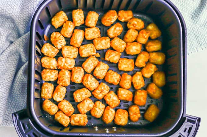 Air Fryer tater tots in an even layer after cooking with a kitchen towel to the side