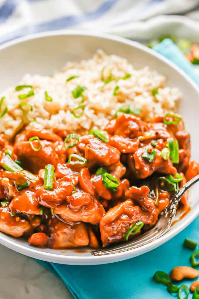 Cashew chicken served with steamed brown rice in a low white bowl with a fork tucked in the side