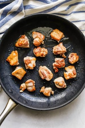 Individual pieces of chicken thighs being seared in oil in a large dark skillet