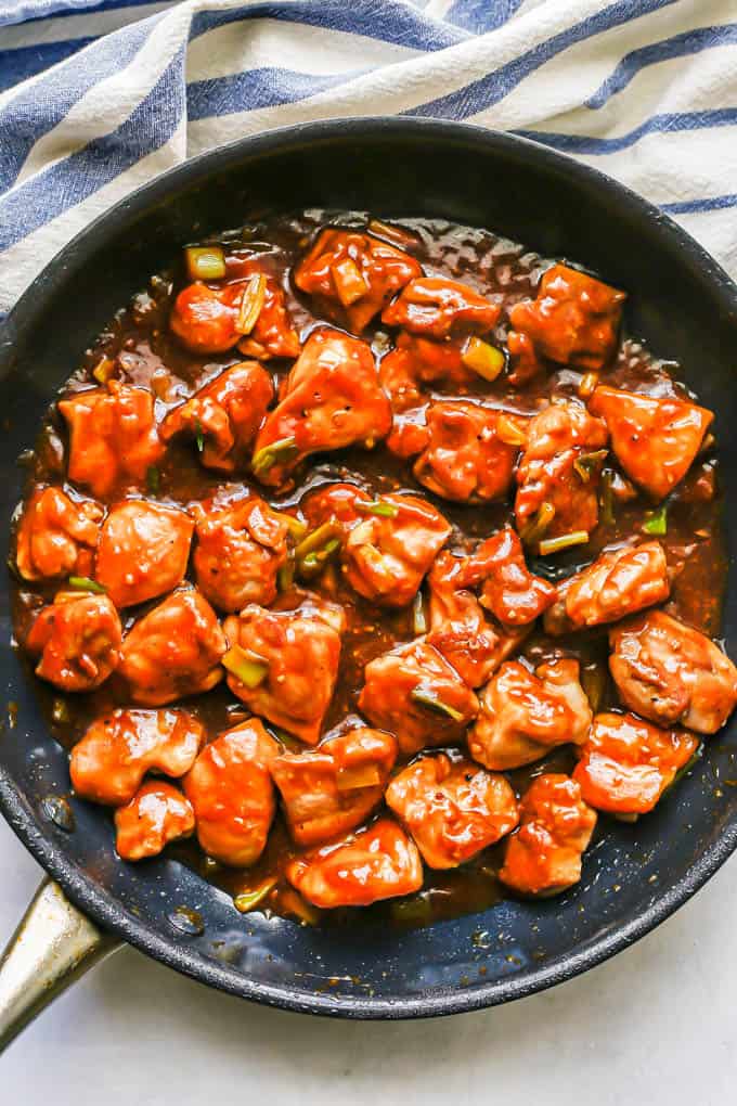 Chunks of chicken thighs being cooked in a light brown sauce in a large skillet