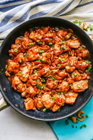 Easy cashew chicken in a large dark skillet with a blue and white striped kitchen towel and turquoise napkins nearby
