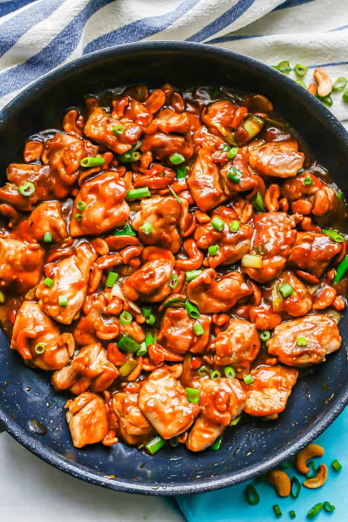Easy cashew chicken in a large dark skillet with a blue and white striped kitchen towel nearby