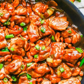 Saucy cashew chicken in a large skillet with green onions on top