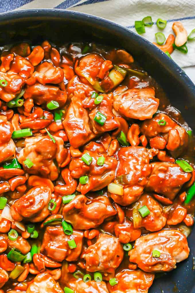Saucy cashew chicken in a large skillet with green onions on top