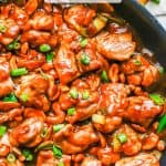 Saucy cashew chicken in a large skillet with green onions on top and a text overlay on the photo