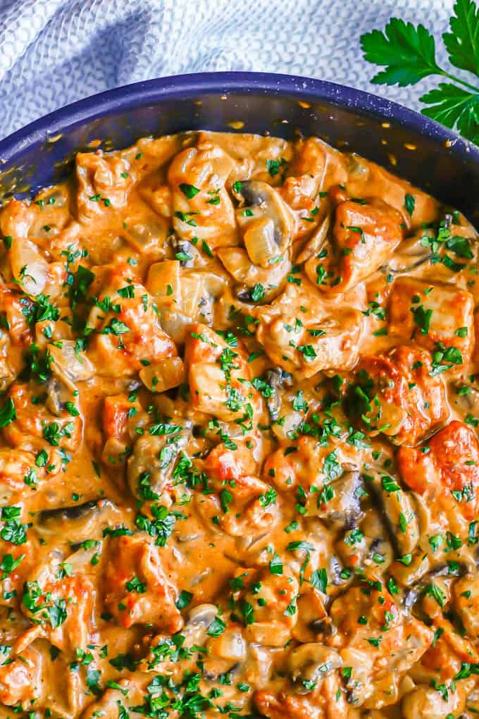 Close up of creamy chicken paprikash in a large skillet with mushrooms and onions mixed in and fresh parsley sprinkled on top