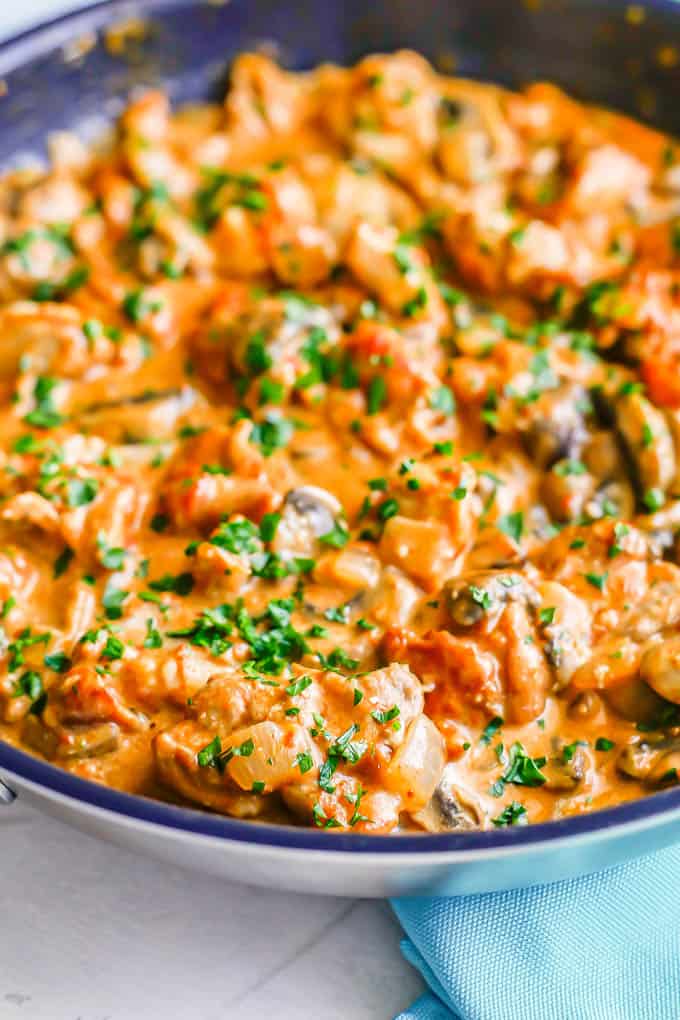 Side angle close-up of creamy chicken paprikash in a large skillet with mushrooms and onions mixed in and fresh parsley sprinkled on top